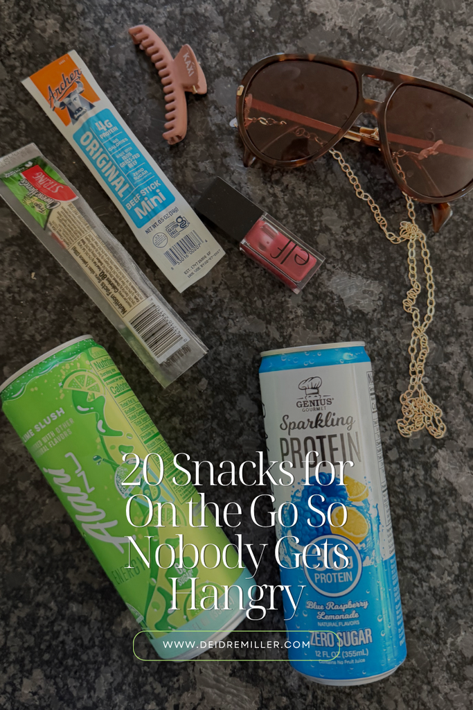 Flat lay of on the go snacks for moms and kids including a beef stick, cheese stick, drink, fruit, and trail mix