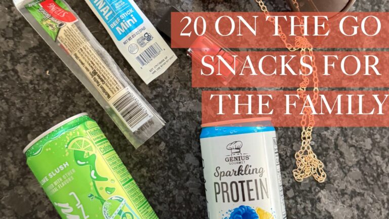 Flat lay of on the go snacks for moms and kids including a beef stick, cheese stick, drink, fruit, and trail mix